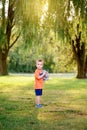 Kid with stuffed plush toy friend. Little cute toddler Caucasian boy in red orange t-shirt holding toy standing alone in park with Royalty Free Stock Photo