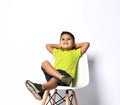 Kid in sunglasses, yellow t-shirt, denim shorts, khaki sneakers. Smiling showing victory sign, sitting on chair. on white