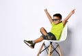 Kid in sunglasses, yellow t-shirt, denim shorts, khaki sneakers. Smiling showing victory sign, sitting on chair.  on white Royalty Free Stock Photo