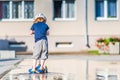 Kid toddler riding his scooter in a city. Summertime fun activity. Caucasian white boy is wearing a hat.