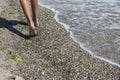 Kid is walking on beach covered with tine stones, seaweeds and wrecked broken shells.