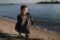 Kid walking on the beach in dark clothes. Warm autumn day. A lonely girl on the river Bank on sunset. Kids Emotions.