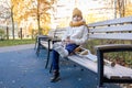 Kid walks in autumn park on crutches. Child sitting on park bench and playing with toys. Girl has one leg broken in cast