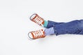 Kid wearing different pair of socks. Child foots in mismatched socks and red sneakers sitting on white background. Odd