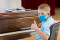 Kid wearing a mask and playing the piano at lesson and event. Kids back to school concept Royalty Free Stock Photo