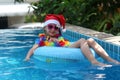 Kid wearing Santa Claus hat are swimming in a blue pool on a bright sunny day and smiling. Concept of happy new year and christmas Royalty Free Stock Photo