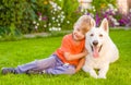 Kid and White Swiss Shepherd dog together on green grass