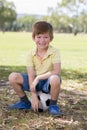 Kid 7 or 8 years old enjoying happy playing football soccer at grass city park field posing smiling proud sitting on the ball in Royalty Free Stock Photo