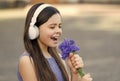 Kiddie song. Happy kid sing song outdoors. Using flowers as microphone. Little child enjoy singing in headphones Royalty Free Stock Photo