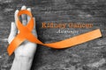 Kidney cancer awareness orange ribbon on human helping hand+ old aged background Royalty Free Stock Photo