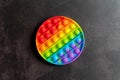 Kids anti stress sensory pop it or simple dimple fidget push toy on a black table or floor background. round popit rainbow hue bri