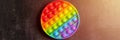 Kids anti stress sensory pop it or simple dimple fidget push toy on a black table or floor background. round popit rainbow hue bri