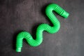 kids anti stress sensory pop tube plastic fidget push toy on a black table or floor background. childrens small poptube toys green