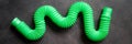 kids anti stress sensory pop tube plastic fidget push toy on a black table or floor background. childrens small poptube toys green