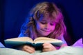 Kids bedtime. Close up portrait of boy reading a book in bed.