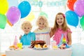 Kids birthday party. Child blowing out candles on colorful cake. Decorated home with rainbow flag banners, balloons. Farm animals