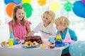 Kids birthday party. Child blowing out candles on colorful cake. Decorated home with rainbow flag banners, balloons. Farm animals Royalty Free Stock Photo