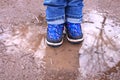 Kids boots in muddy puddle. Colorful winter outdoor rain shoes on childrens feet in action. A child on stay in the mud Royalty Free Stock Photo