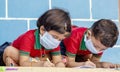 Kids busy in writing with medical face mask wearing due to covid-19 or coronavirus outbreak or pandemic at school -