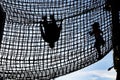 Kids climbing inside a rope net high in the sky - girl walking and boy hanging upside down - silhouettes