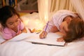 Kids, color pencil and drawing on bed for sleepover, creative and relax in bedroom for weekend. Young girls, playing and Royalty Free Stock Photo