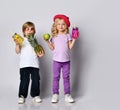 Kids in colorful casual clothes. Smiling, holding yellow and pink cocktail bottles, apple, pineapple. Posing isolated on white