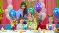 Kids in colorful hats celebrating birthday with mother and fiends.