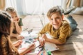 Kids drawing on paper with pencils while lying on floor