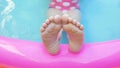 Kids feet dancing on in colorful rainbow inflatable swimming pool. Young girl in pink swimsuit playing in water 4K