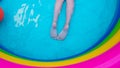 Kids feet laying on colorful rainbow inflatable swimming pool. Young girl relaxing and playing in water on a backyard Royalty Free Stock Photo