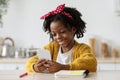 Cute African American Girl Using Smartphone While Sitting At Table In Kitchen Royalty Free Stock Photo