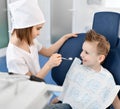 Kids girl and boy play dentist and patient in dental office. Boy is in dental chair and dentist starts check with a dental mirror Royalty Free Stock Photo