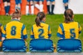 Kids girls elementary school sports team sitting on bench on the grass field. Soccer football junior girls team