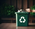 Kids hand putting garbage into a trash bin filled with waste paper ready for recycling, natural wooden background with green Royalty Free Stock Photo