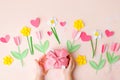 Kids hands holding gift present box with pink bow decorated paper hearts and tulip flowers on pink pastel table top view. Flat lay