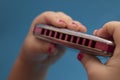 Kids hands holding red harmonica, close-up. Blue background Royalty Free Stock Photo