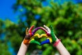 Kids hands painted in bright colors make a heart shape on summer nature background Royalty Free Stock Photo