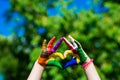 Kids hands painted in bright colors make a heart shape on summer nature background Royalty Free Stock Photo