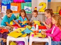 Kids holding colored paper on table in kindergarten .