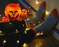 Kids legs in stylish warm bright colorful striped funny socks in garland lights on floor with pumpkins in room.