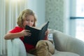 Kids and literature. Child reading book, sitting at home in cozy living room on couch. Concept of education, childhood Royalty Free Stock Photo