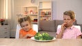 Kids looking with disgust at broccoli, unappetizing meal, tasteless healthy food Royalty Free Stock Photo