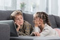 Preschooler children lying on a sofa with a laptop and looking at each