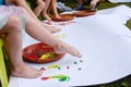 Kids colour painting with their foot on a white paper