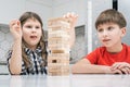 Kids play jenga sitting at table. Boy and girl with concentrated facial expression build tower from wooden blocks.