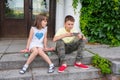 Kids play outside. A boy and a girl are sitting on the steps with a phone in their hands. Hipsters Royalty Free Stock Photo