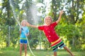 Kids play with water sprinkle hose. Summer garden