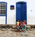 Kids playing around in front of a blue door of a white building in the old town of Paraty in Brazil