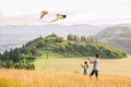 Kids playing: sister with a brother with launching colorful kites - popular outdoor toy on the high grass hills meadow. Happy