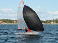 Kids racing a small sailboat with a Black spinnaker at a Junior yachting regatta on a coastal lake Royalty Free Stock Photo